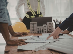 Consult People viewing and pointing to a building design on a desk with rulers, pencils and a hard hat.