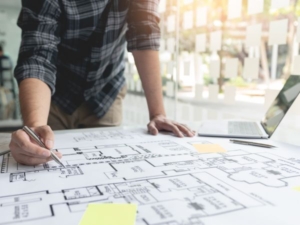 Design Someone has large print out of a building's layout, with sticky notes, a laptop and pens.