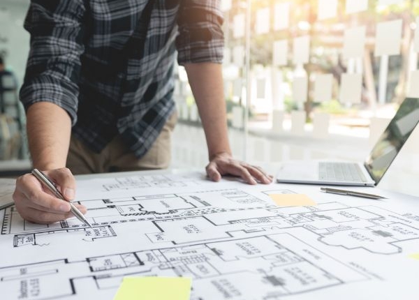 Design Someone has large print out of a building's layout, with sticky notes, a laptop and pens.