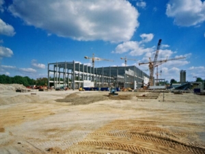 Build a large industrial steel building being constructed with cranes and industrial trucks