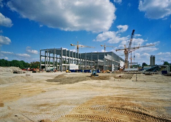 Build a large industrial steel building being constructed with cranes and industrial trucks